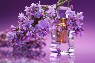 Photo of Bottle of perfume and branch with lilac flowers on mirror surface against color gradient background, closeup
