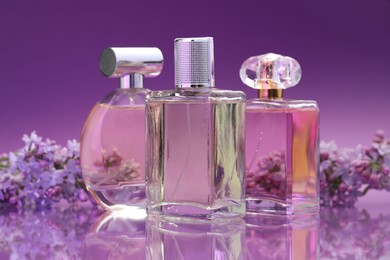 Photo of Bottles with perfumes and lilac flowers on mirror surface against color gradient background, closeup