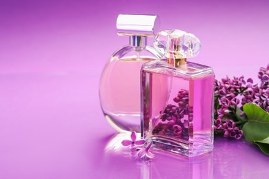 Photo of Bottles with perfumes and lilac flowers on mirror surface against color gradient background, closeup. Space for text
