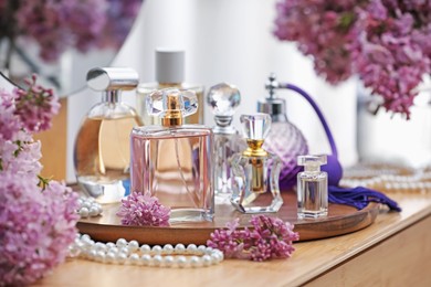 Photo of Bottles with perfumes and lilac flowers on dressing table indoors, closeup