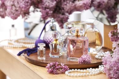 Photo of Bottles with perfumes and lilac flowers on dressing table indoors, closeup