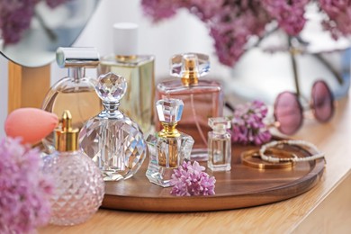 Photo of Bottles with perfumes and lilac flowers on dressing table indoors, closeup