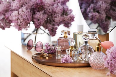 Photo of Bottles with perfumes, lilac flowers and accessories on dressing table indoors, closeup