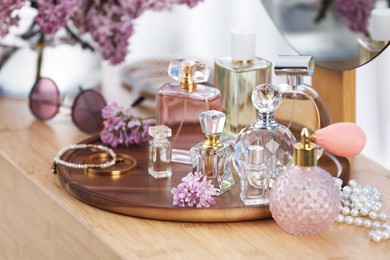 Photo of Bottles with perfumes, lilac flowers and accessories on dressing table indoors, closeup