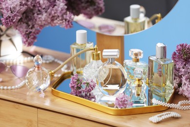 Photo of Bottles with perfumes, lilac flowers and accessories on dressing table indoors