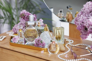 Photo of Bottles with perfumes, lilac flowers and accessories on dressing table indoors