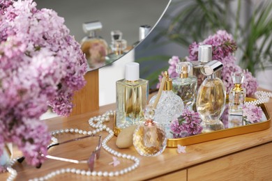 Photo of Bottles with perfumes, lilac flowers and accessories on dressing table indoors