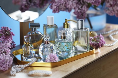 Photo of Bottles with perfumes, lilac flowers and accessories on dressing table indoors