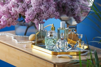 Photo of Bottles with perfumes, lilac flowers and accessories on dressing table indoors