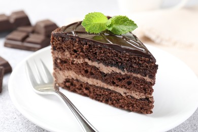 Photo of Piece of delicious chocolate cake with mint and fork on table, closeup