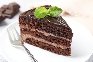 Photo of Piece of delicious chocolate cake with mint and fork on table, closeup