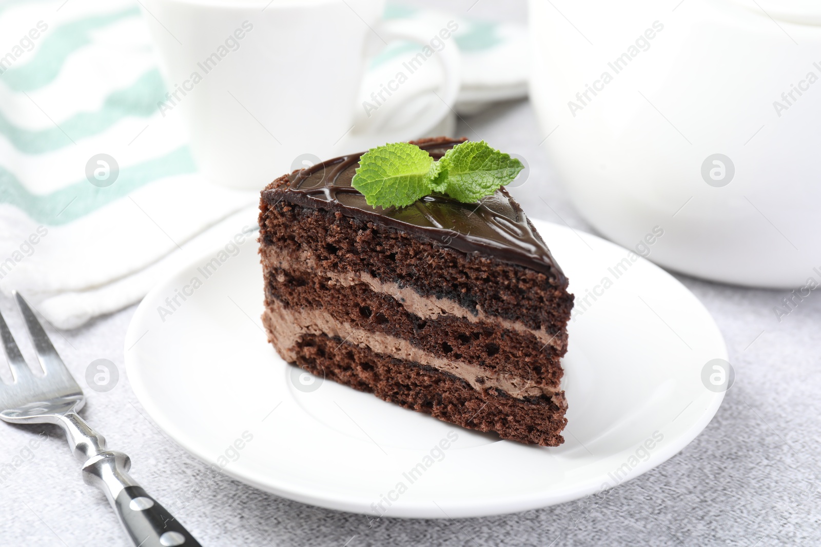 Photo of Piece of delicious chocolate cake with mint and fork on grey table, closeup