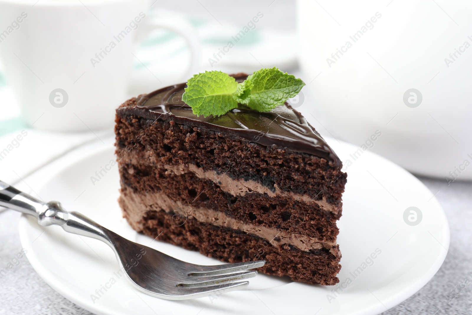 Photo of Piece of delicious chocolate cake with mint and fork on table, closeup