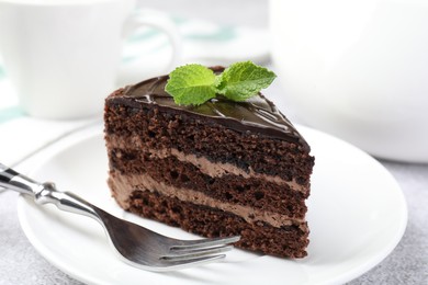 Photo of Piece of delicious chocolate cake with mint and fork on table, closeup
