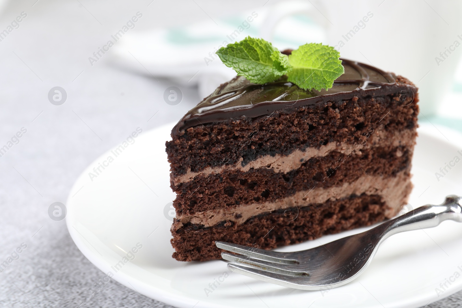 Photo of Piece of delicious chocolate cake with mint and fork on grey table, closeup