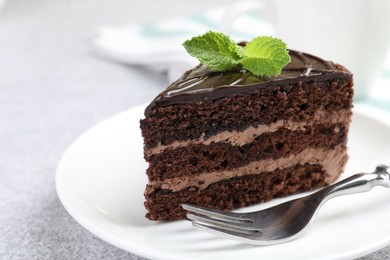 Photo of Piece of delicious chocolate cake with mint and fork on grey table, closeup