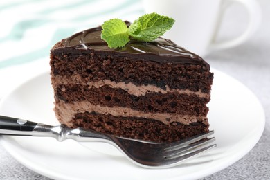 Photo of Piece of delicious chocolate cake with mint and fork on table, closeup
