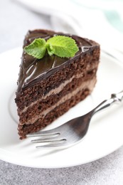 Photo of Piece of delicious chocolate cake with mint and fork on grey table, closeup