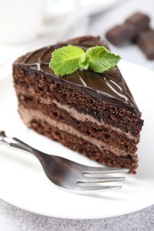 Photo of Piece of delicious chocolate cake with mint and fork on table, closeup