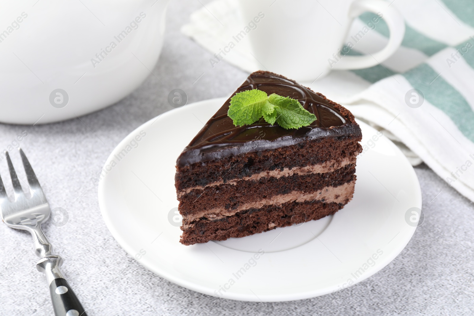 Photo of Piece of delicious chocolate cake with mint and fork on grey table, closeup