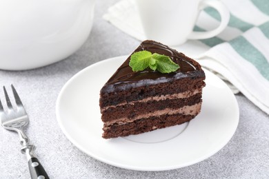 Photo of Piece of delicious chocolate cake with mint and fork on grey table, closeup