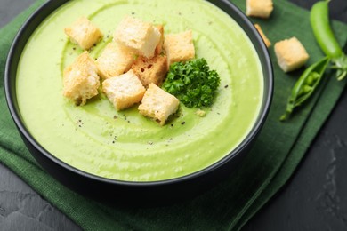 Photo of Tasty pea cream soup with croutons and broccoli served on black table, closeup