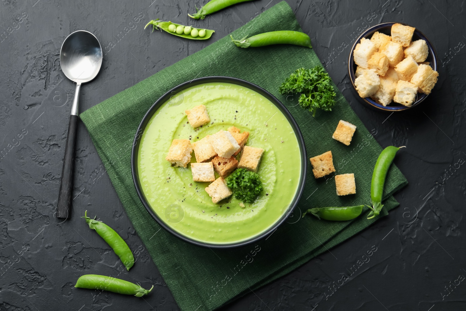 Photo of Tasty pea cream soup with croutons and broccoli served on black table, flat lay