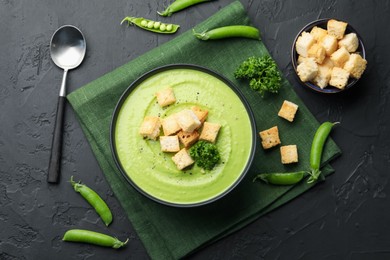 Photo of Tasty pea cream soup with croutons and broccoli served on black table, flat lay