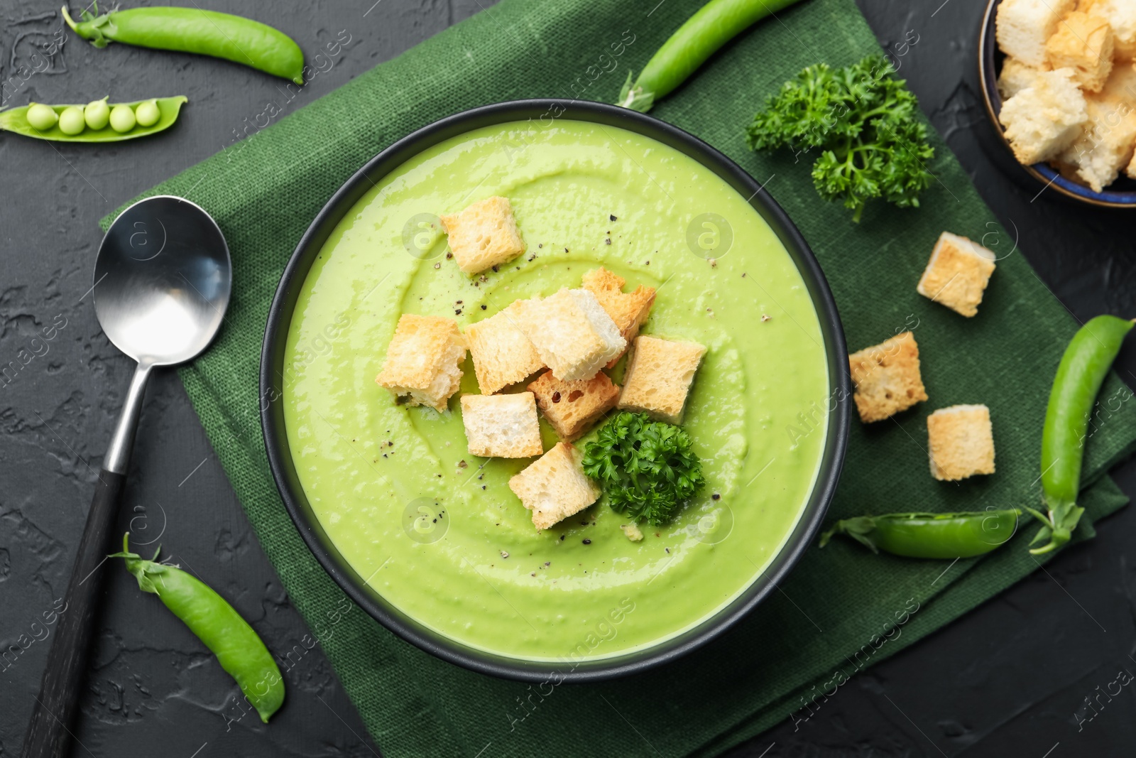 Photo of Tasty pea cream soup with croutons and broccoli served on black table, flat lay