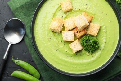 Photo of Tasty pea cream soup with croutons and broccoli served on black table, flat lay