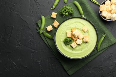 Photo of Tasty pea cream soup with croutons and broccoli served on black table, flat lay. Space for text