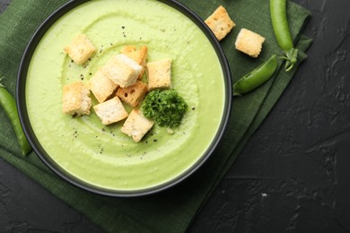 Photo of Tasty pea cream soup with croutons and broccoli served on black table, flat lay