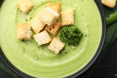 Photo of Tasty pea cream soup with croutons and broccoli on black table, top view