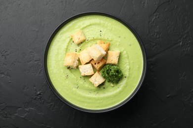 Photo of Tasty pea cream soup with croutons and broccoli on black table, top view