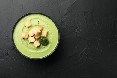 Photo of Tasty pea cream soup with croutons and broccoli on black table, top view. Space for text