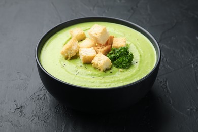 Photo of Tasty pea cream soup with croutons and broccoli on black table, closeup