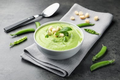 Photo of Tasty pea cream soup with croutons, basil and microgreens served on grey table