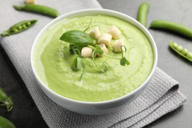 Photo of Tasty pea cream soup with croutons, basil and microgreens served on grey table, closeup