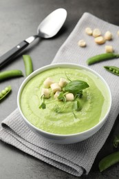 Photo of Tasty pea cream soup with croutons, basil and microgreens served on grey table