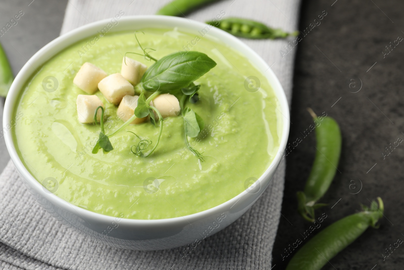 Photo of Tasty pea cream soup with croutons, basil and microgreens served on grey table, closeup