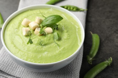Photo of Tasty pea cream soup with croutons, basil and microgreens served on grey table, closeup
