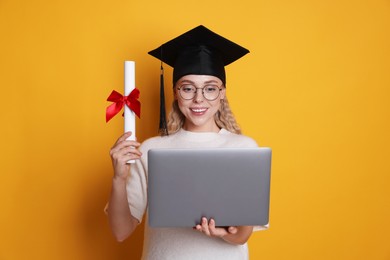 Photo of Happy student with diploma and laptop after graduation on orange background