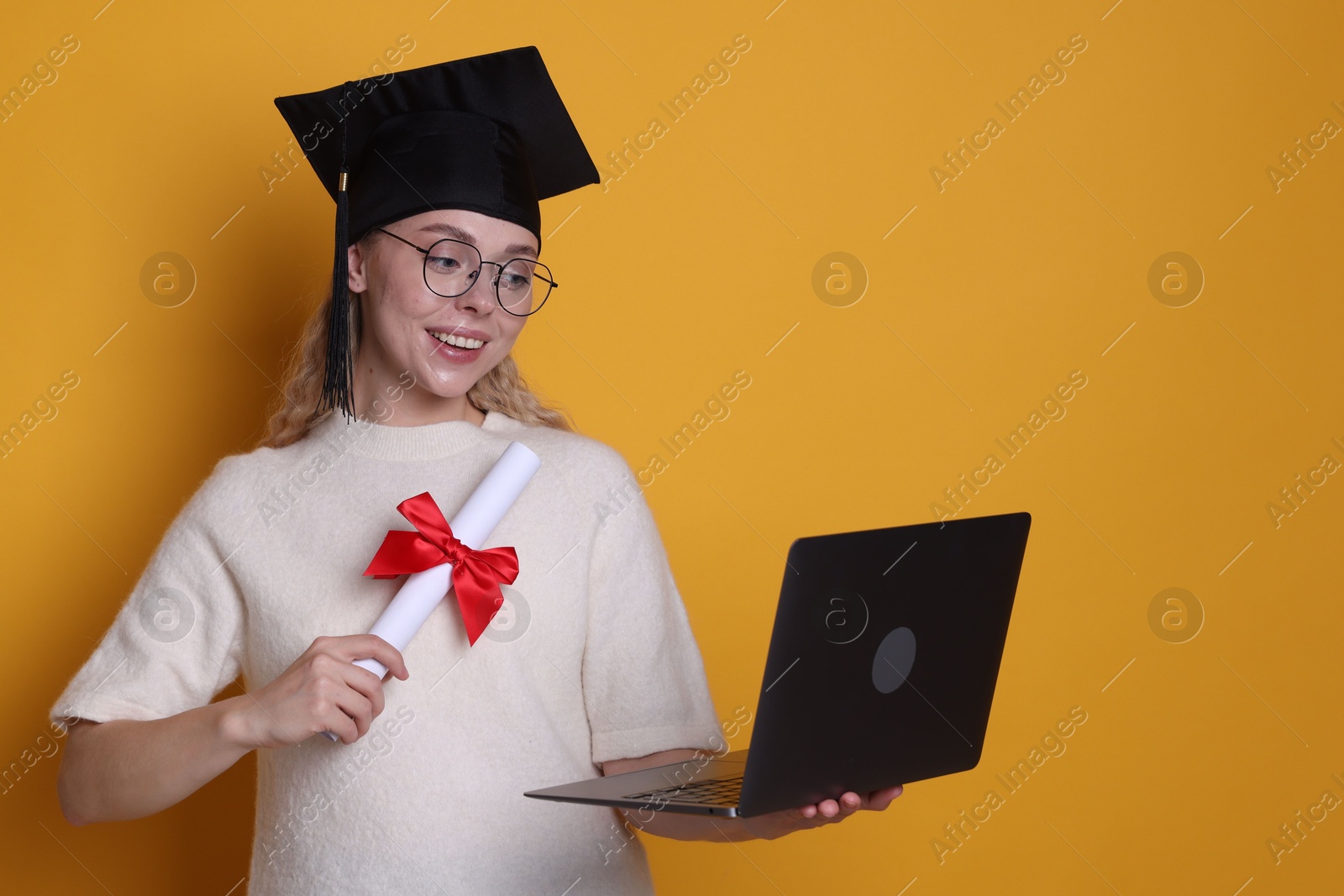 Happy student with diploma and laptop after graduation on orange background Photo of Happy student with diploma and laptop after graduation on orange background