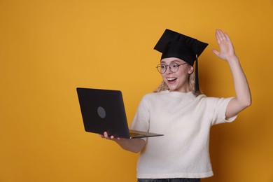 Photo of Happy student with laptop waving hello after graduation on orange background