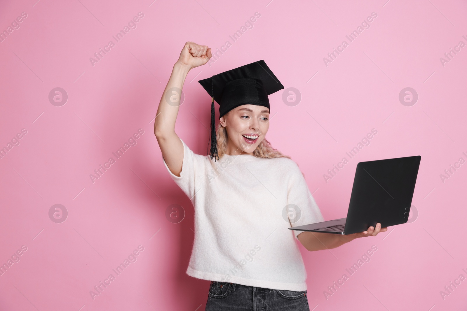 Happy student with laptop after graduation on pink background Photo of Happy student with laptop after graduation on pink background
