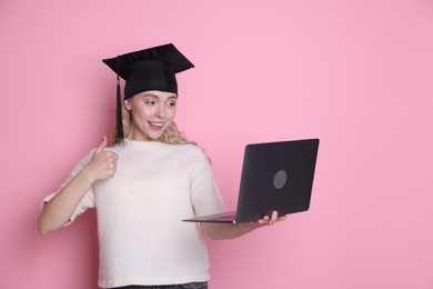 Photo of Happy student with laptop showing thumbs up after graduation on pink background