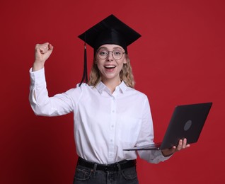 Photo of Happy student with laptop after graduation on red background