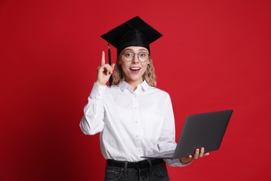 Photo of Happy student with laptop after graduation on red background
