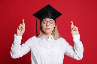 Photo of Emotional student crossing fingers on red background. Hope for good graduation