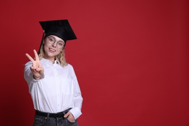 Photo of Happy student showing peace sign after graduation on red background. Space for text